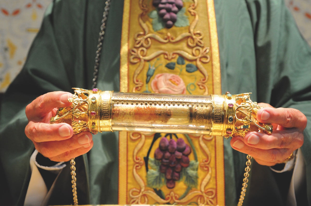cleric carrying the relic of the Holy Blood: piece of cloth with blood of Christ, contained in a glass cylinder with a gold-colored metal setting at both ends
