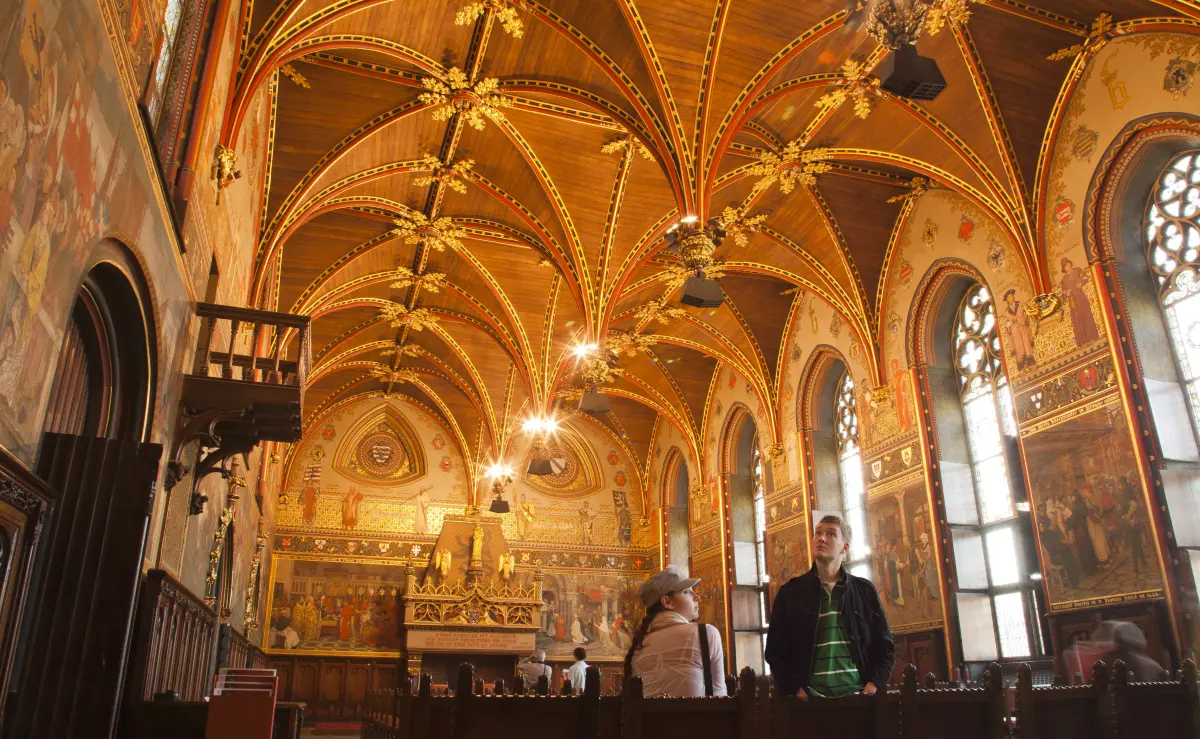 Two visitors are looking around in the Gothic Hall with murals and a polychrome vault